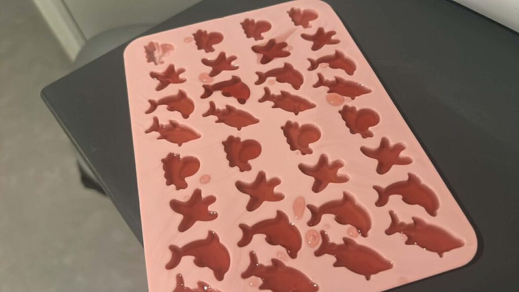 Moule en silicone rose rempli de gélatine en forme de dauphins et d'étoiles de mer