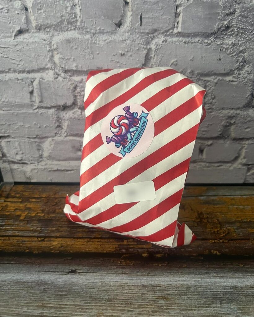 Sachet emballé dans un papier rayé rouge et blanc, fermé par l'autocollant DomConfiserie